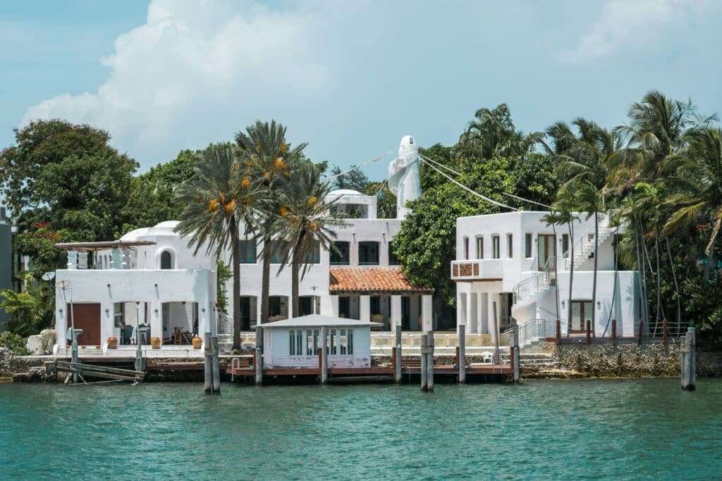 White coastal houses with palm trees along a turquoise water canal and docks in front.