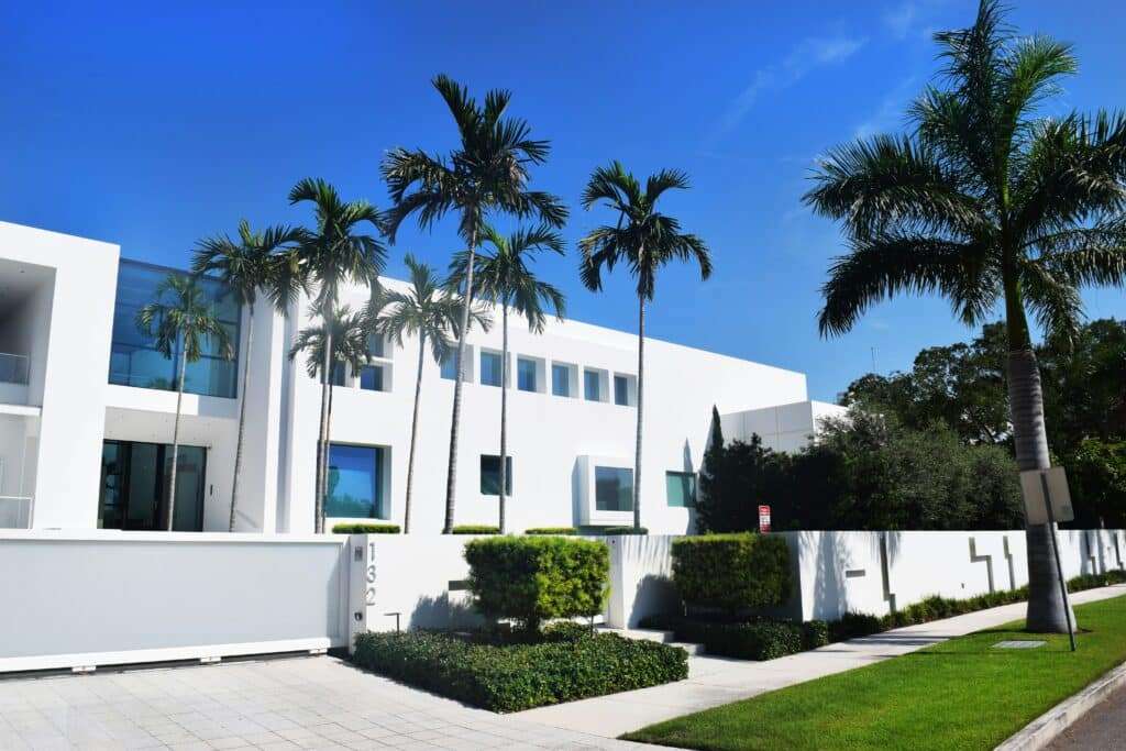 Modern white building with large windows and tall palm trees beneath a bright blue sky.