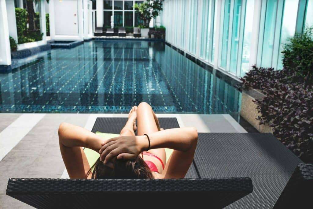 Person lounging on a chair by an indoor pool in a glass-walled atrium