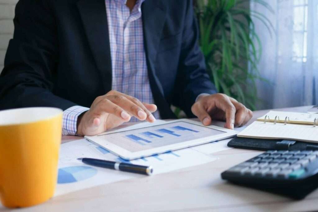 Hands of a person in a dark suit reviewing charts on a desk with a yellow mug in the foreground.