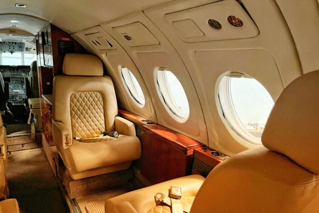 Interior of a private jet cabin with beige quilted leather seats and wooden trim along the windows