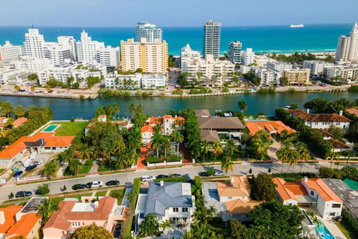 Aerial view of luxury waterfront homes in South Florida with a canal, palm-lined properties, and the Atlantic Ocean beyond