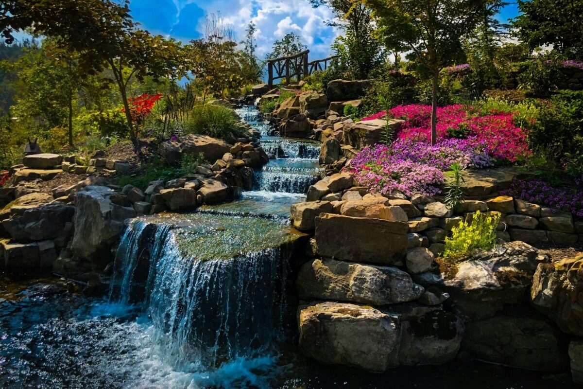 Luxury landscape architecture featuring a cascading waterfall, natural stone terraces, vibrant gardens, and mature trees