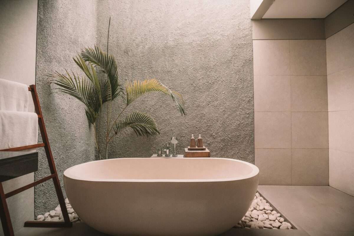 Luxury spa bathroom with freestanding soaking tub, natural stone and tropical greenery