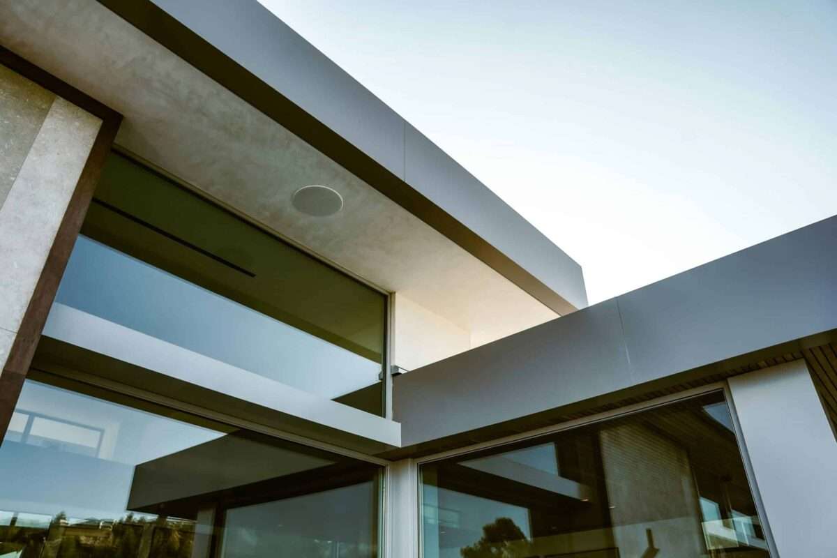 Modern luxury home exterior featuring clean architectural lines, expansive floor-to-ceiling glass, cantilevered roof design, and premium contemporary construction.