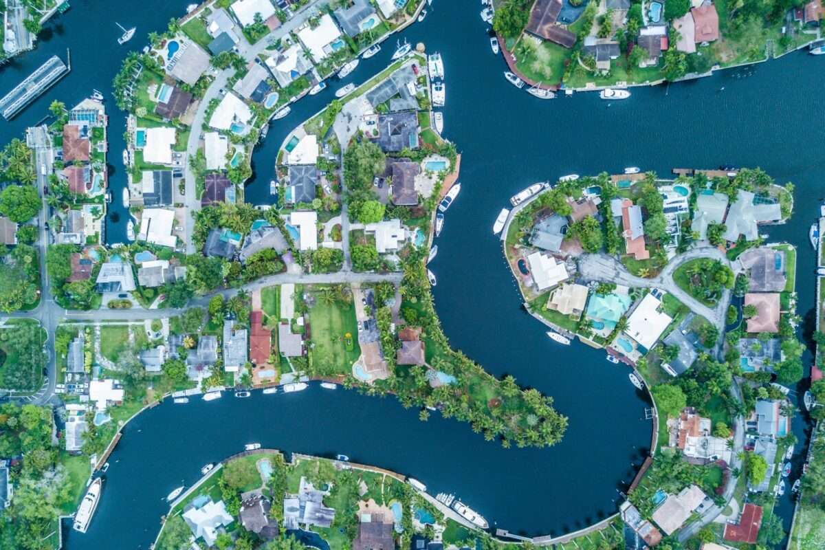 Aerial view of South Florida waterfront homes on narrow lots surrounded by canals, docks, boats, pools, and tropical landscaping