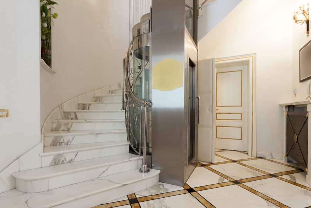 Residential elevator beside a curved marble staircase in a luxury home