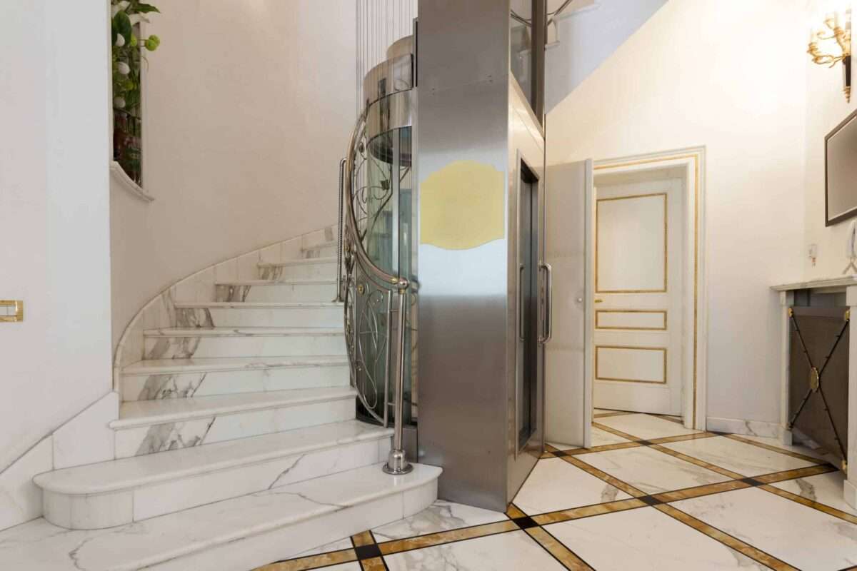 Residential elevator beside a curved marble staircase in a luxury home