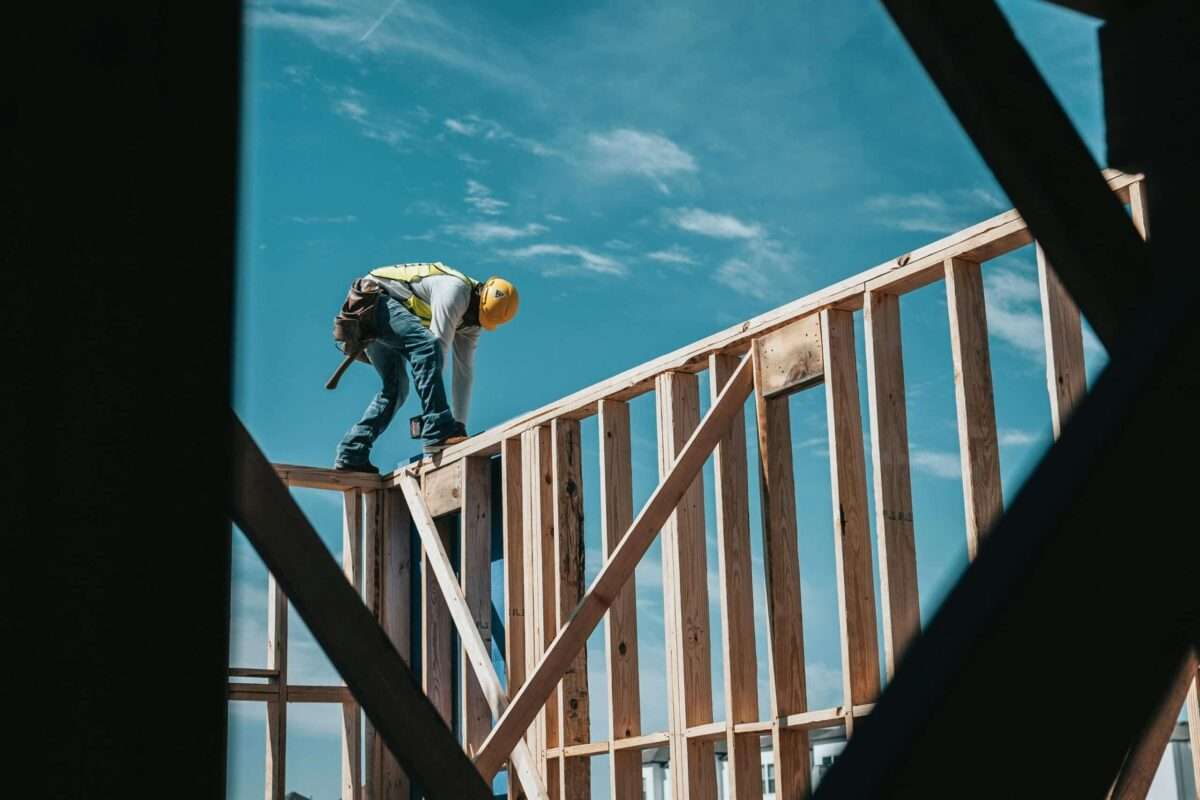 Construction worker framing a luxury home addition under a clear blue sky