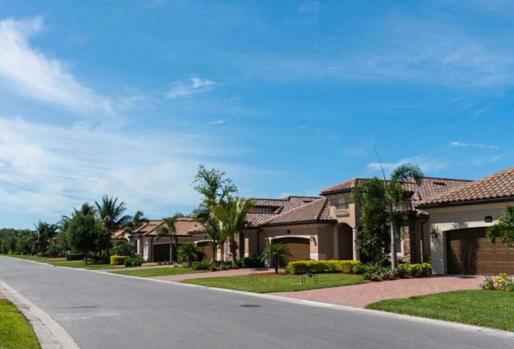 Mediterranean-style homes with tile roofs, palm trees and landscaped front yards along a residential street.