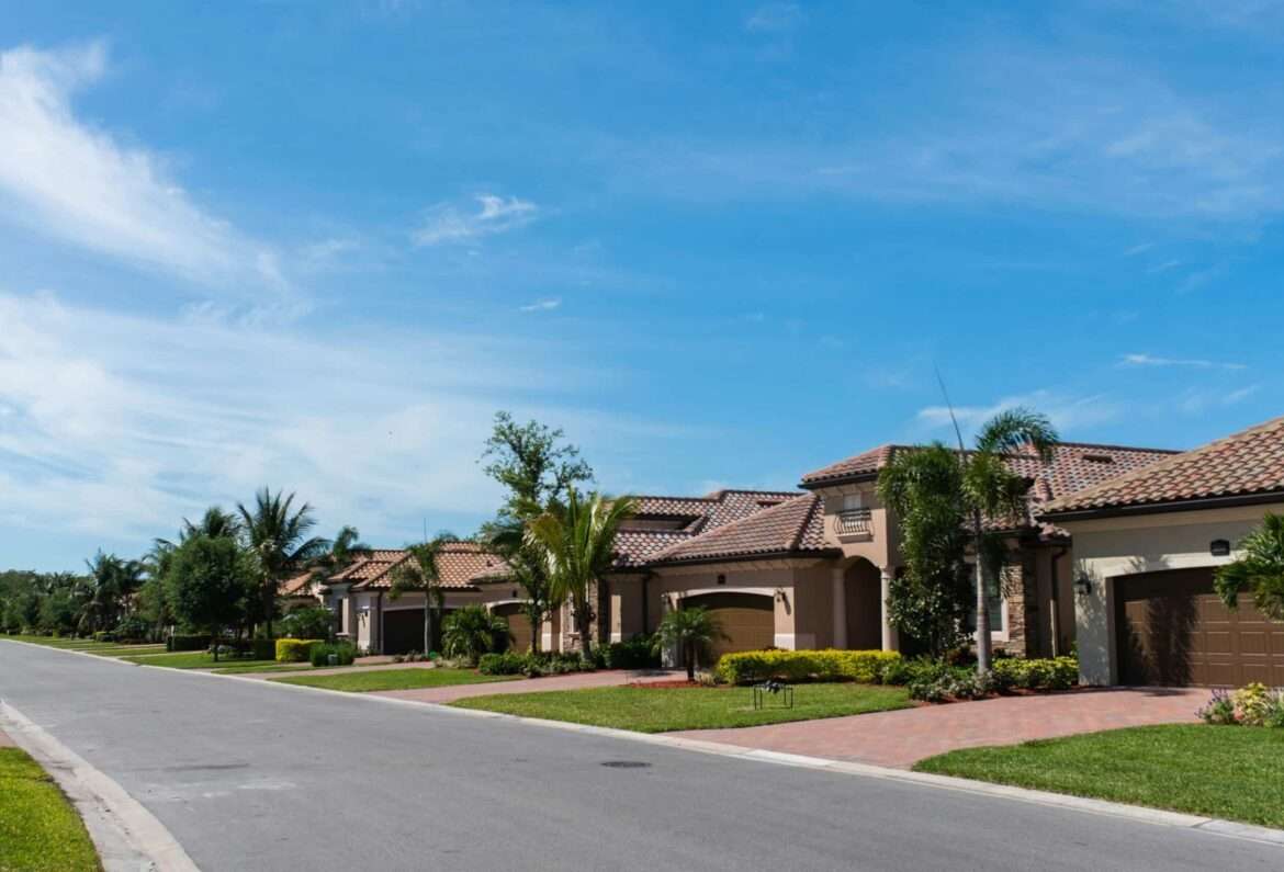 Mediterranean-style homes with tile roofs, palm trees and landscaped front yards along a residential street.