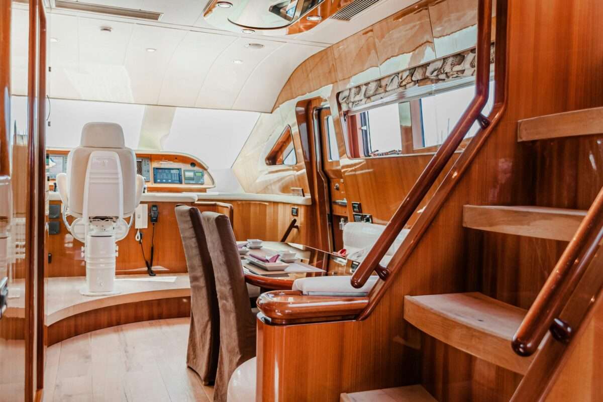 Luxury yacht interior with polished wood finishes, a helm station, dining area and staircase