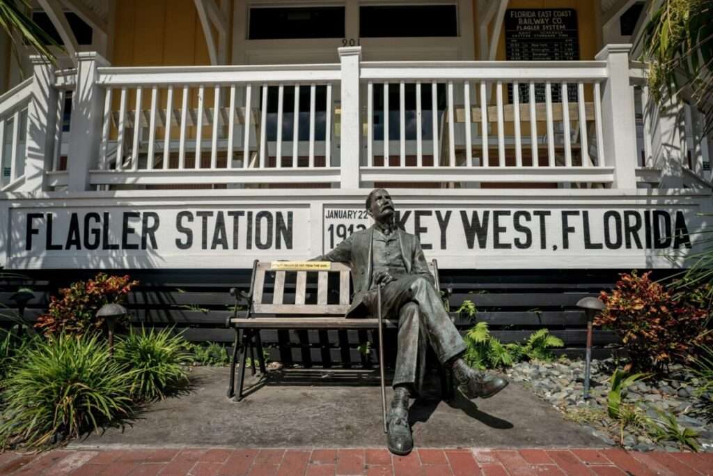 Seated bronze statue outside Flagler Station in Key West, Florida, with historic railway signage and tropical landscaping.