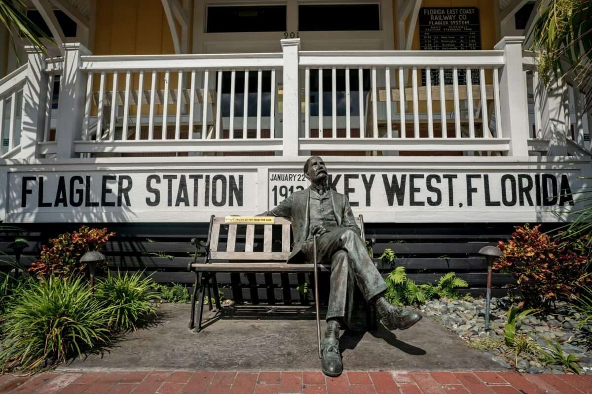 Seated bronze statue outside Flagler Station in Key West, Florida, with historic railway signage and tropical landscaping.